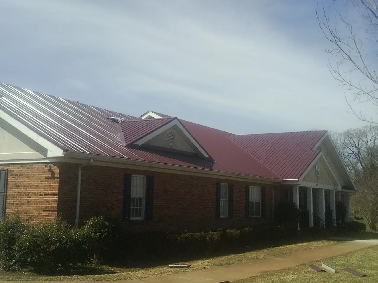 Red metal roof with gabled entries on a long brick building, from a Hail Damage Roof Repair job in Mercersburg