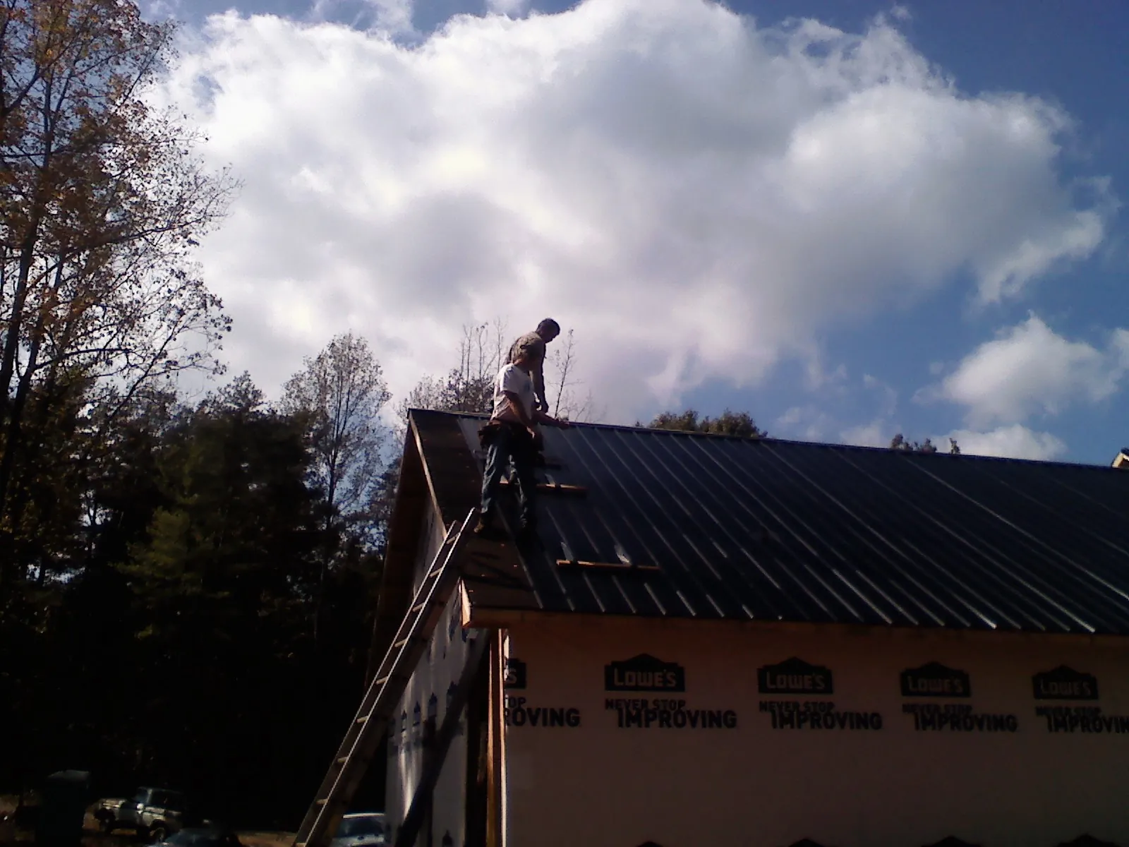 Roofer fastening dark metal panels high against a cloudy sky, from a Roof Inspection job in Mercersburg