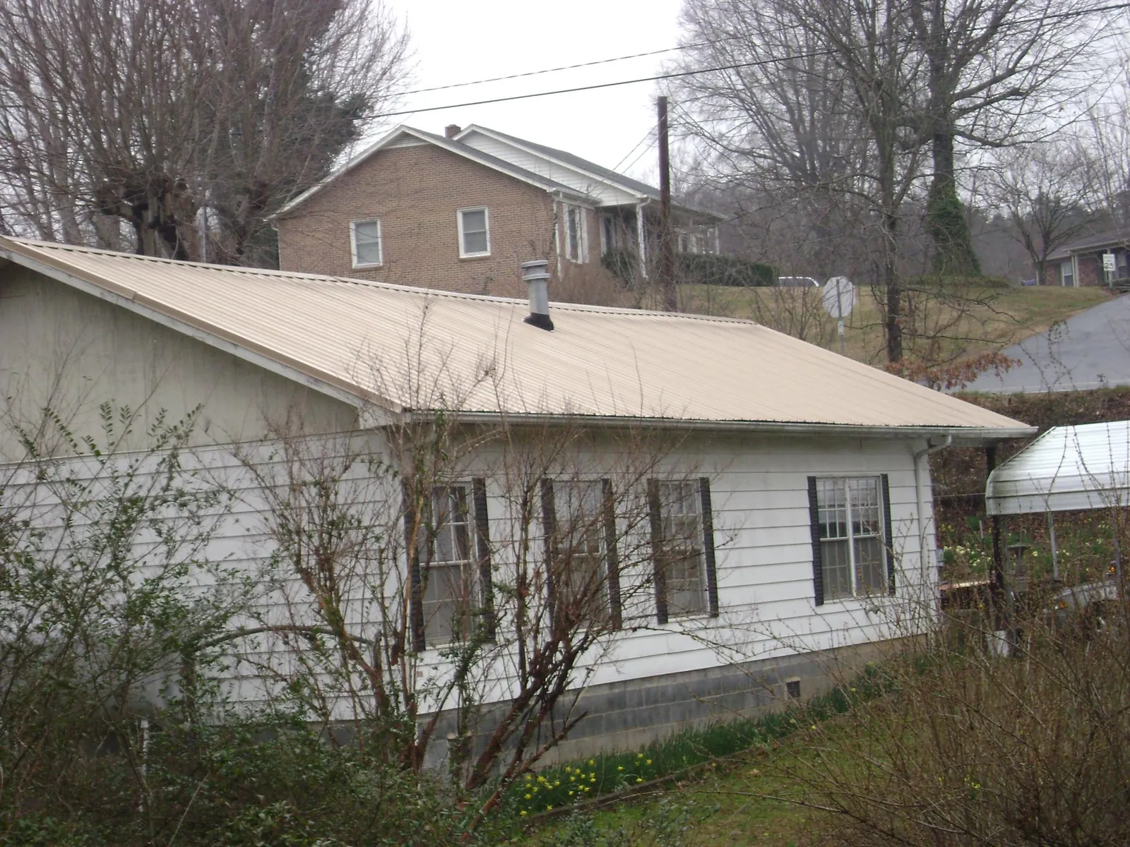Tan metal roof on a white sided house set into a hillside — Commercial Roofing by Roofing Brothers in Mercersburg